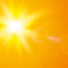 En bländande nysa av solen lyser upp en varm, orange bakgrund med strålar och linsöverstrålning.
