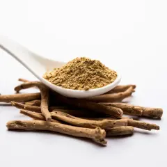 Ashwagandha-rotpulver på en sked över en hög med torkade rötter. Vissa användare rapporterar ashwagandha biverkningar, såsom magbesvär.