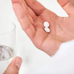 Person håller två vita tabletter i handen, redo att svälja dem med ett glas vatten. Man bör vara medveten om eventuella madopark biverkningar.