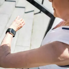 Äldre kvinna kollar sin smartklocka, som kan användas för långtids ekg, efter ett träningspass utomhus.