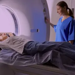 En patient ligger på en brits i en MR-scanner, medan en sjuksköterska justerar inställningarna. Mr Ryggs undersökning pågår.