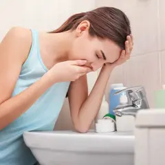Gravid kvinna med illamående vid handfatet, hon håller handen för munnen. Kanske behöver hon medicin.