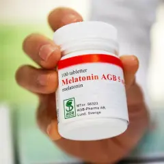 En hand håller en burk med 100 melatonin tabletter. Frågan "hur mycket melatonin kan man ta" kan besvaras genom att läsa etiketten.