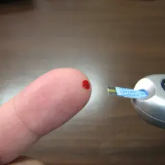 Blodsdroppe på fingret redo för mätning av blodsocker fastande med glukosmätare.