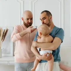 Två pappor kollar febern på sitt koksalt bebis med en termometer.