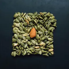 En ensam mandel bland pumpafrön. Kan vara en visuell metafor för e-vitamin brist symptom, då frön är rika på vitamin E.