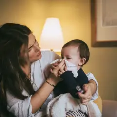 Mamma torkar sin bebis näsa med en pappersnäsduk. Små **indragningar barn** kan vara jobbiga, men mamma finns där för att trösta.