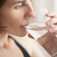 Kvinna dricker vatten ur ett glas, en enkel huskur mot muntorrhet.