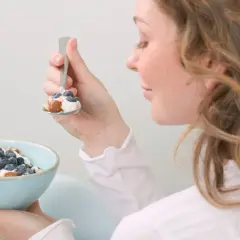 En kvinna äter en skål med yoghurt, blåbär och nötter. En hälsosam frukost som passar bra för diabetes typ 2 kost.