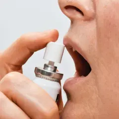 En person använder nitroglycerin spray under tungan för snabb lindring.