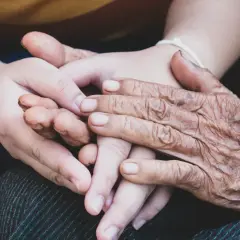 Två händer, en ung och en gammal, flätas samman. Den äldre handen visar tydliga tecken på biologisk ålder, medan den yngre är slät och mjuk. En symbol för livets gång och generationer.