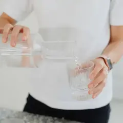 En person häller upp vatten från en glasflaska till ett glas. En hälsosam dryck som mot rethosta.