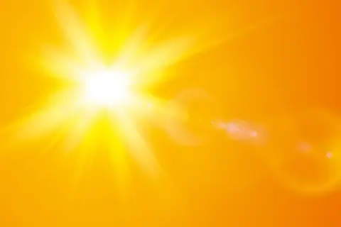 En bländande nysa av solen lyser upp en varm, orange bakgrund med strålar och linsöverstrålning.