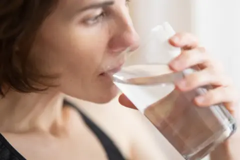 Kvinna dricker vatten ur ett glas, en enkel huskur mot muntorrhet.