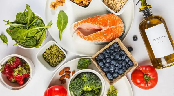 En vacker uppdukning av ingredienser för antiinflammatorisk kost: lax, bär, grönsaker, nötter och olivolja.