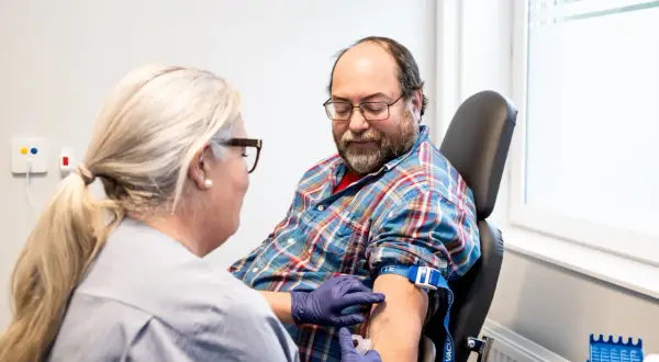 Sjuksköterska tar blodprov på man. Frågan om man kan ta blodtrycksmedicin innan provtagning är viktig för att få korrekta resultat.