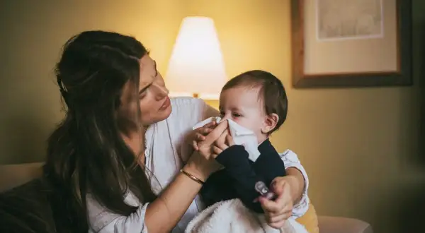Mamma torkar sin bebis näsa med en pappersnäsduk. Små **indragningar barn** kan vara jobbiga, men mamma finns där för att trösta.
