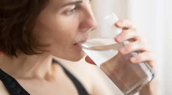 Kvinna dricker vatten ur ett glas, en enkel huskur mot muntorrhet.