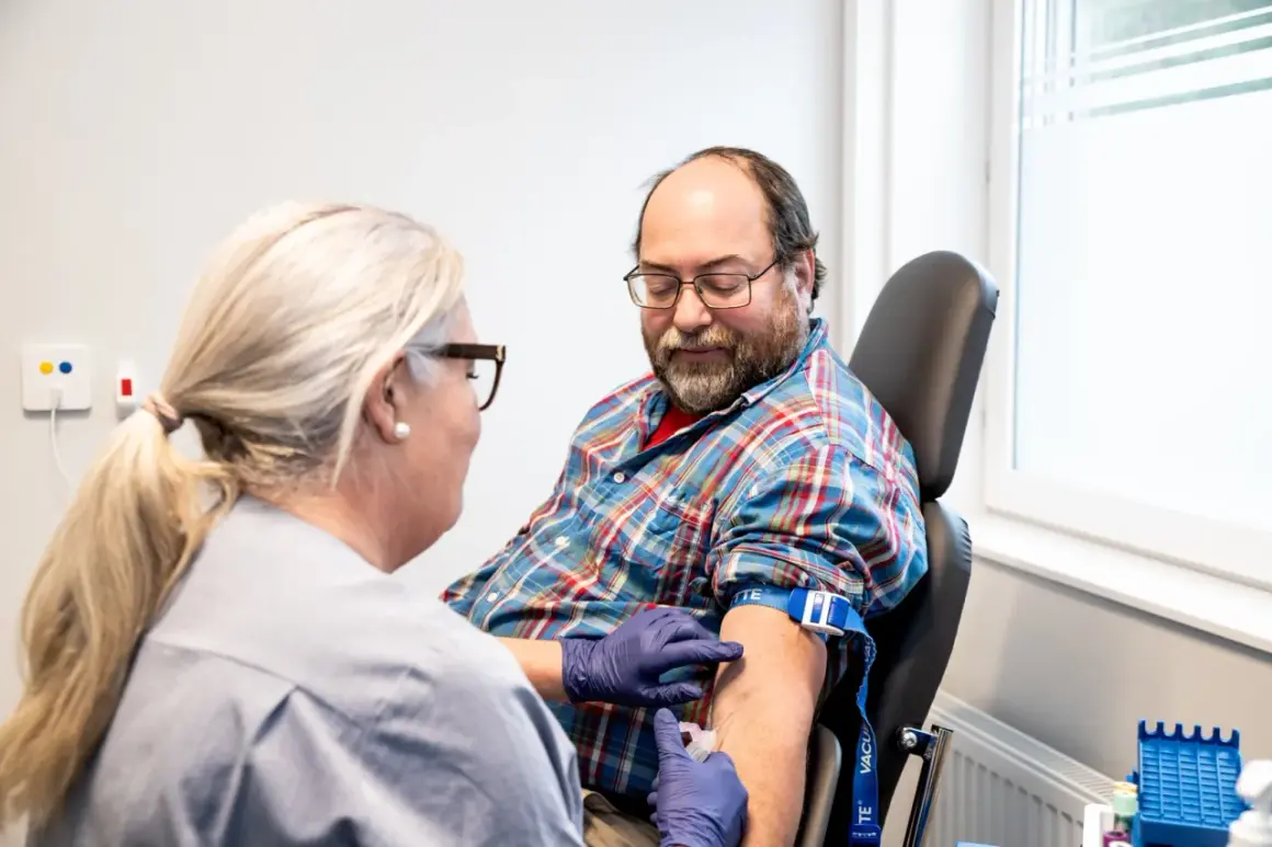 Sjuksköterska tar blodprov på man. Frågan om man kan ta blodtrycksmedicin innan provtagning är viktig för att få korrekta resultat.