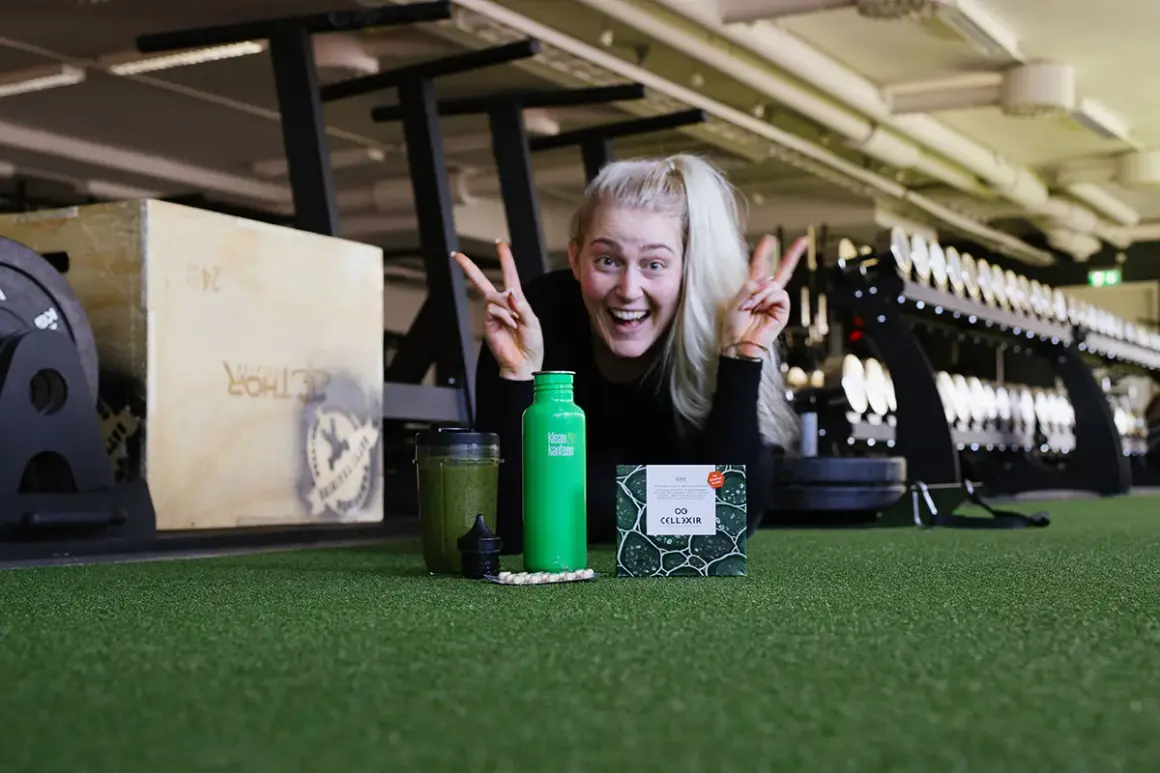 Glad kvinna med energi i gymmet, redo att ta sig an dagen. Frågan är: hur blir man pigg? Kanske med en grön smoothie och kosttillskott?