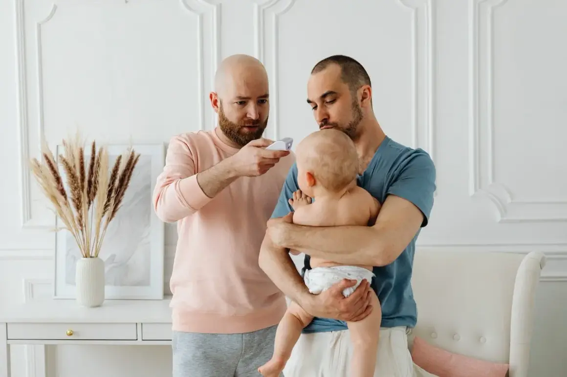 Två pappor kollar febern på sitt koksalt bebis med en termometer.