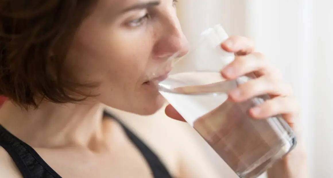 Kvinna dricker vatten ur ett glas, en enkel huskur mot muntorrhet.