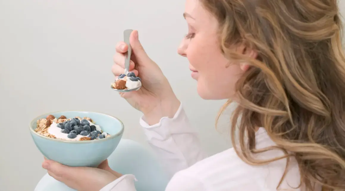 En kvinna äter en skål med yoghurt, blåbär och nötter. En hälsosam frukost som passar bra för diabetes typ 2 kost.