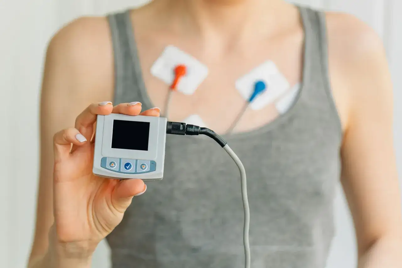 Person med elektroder på bröstet för ett långtids ekg. Håller upp den lilla inspelningsenheten.