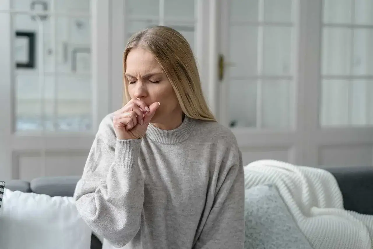 Kvinna med blundade ögon hostar i handen, söker lindring från hosta.