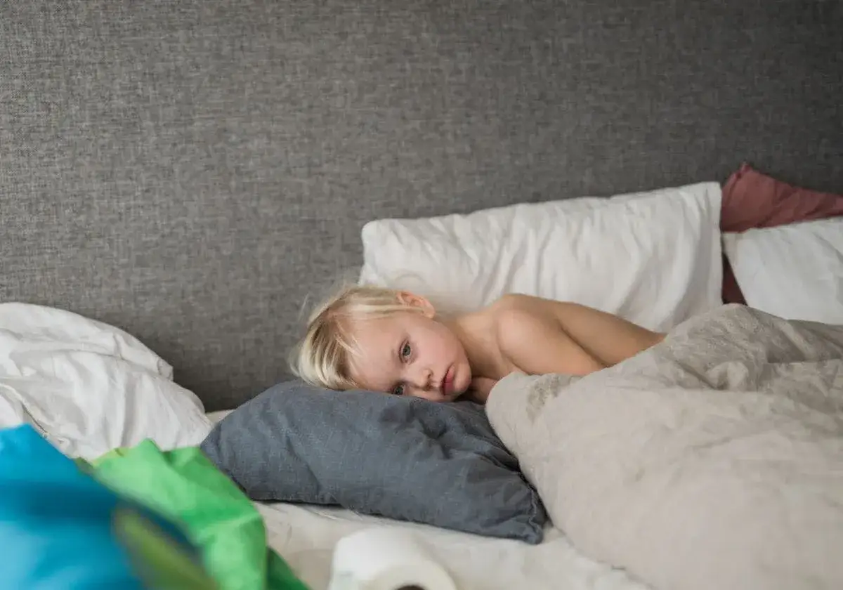 Tr&ouml;tt litet barn med svullna halsmandlar ligger i s&auml;ngen, omgiven av kuddar och t&auml;cken.