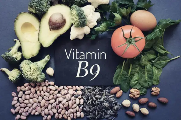 En tavla med texten "Vitamin B9" omgiven av matvaror som broccoli, avokado, bönor, solrosfrön, nötter, spenat, tomat och ägg.