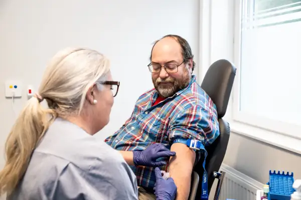 Sjuksköterska tar blodprov på man. Frågan om man kan ta blodtrycksmedicin innan provtagning är viktig för att få korrekta resultat.