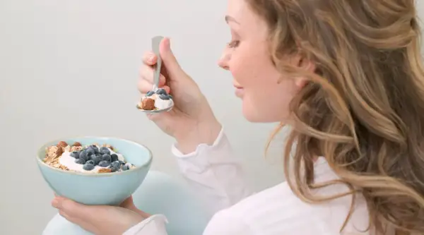 En kvinna äter en skål med yoghurt, blåbär och nötter. En hälsosam frukost som passar bra för diabetes typ 2 kost.